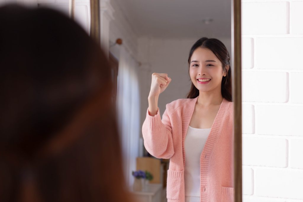 A confident woman in a pink cardigan looking into a mirror
