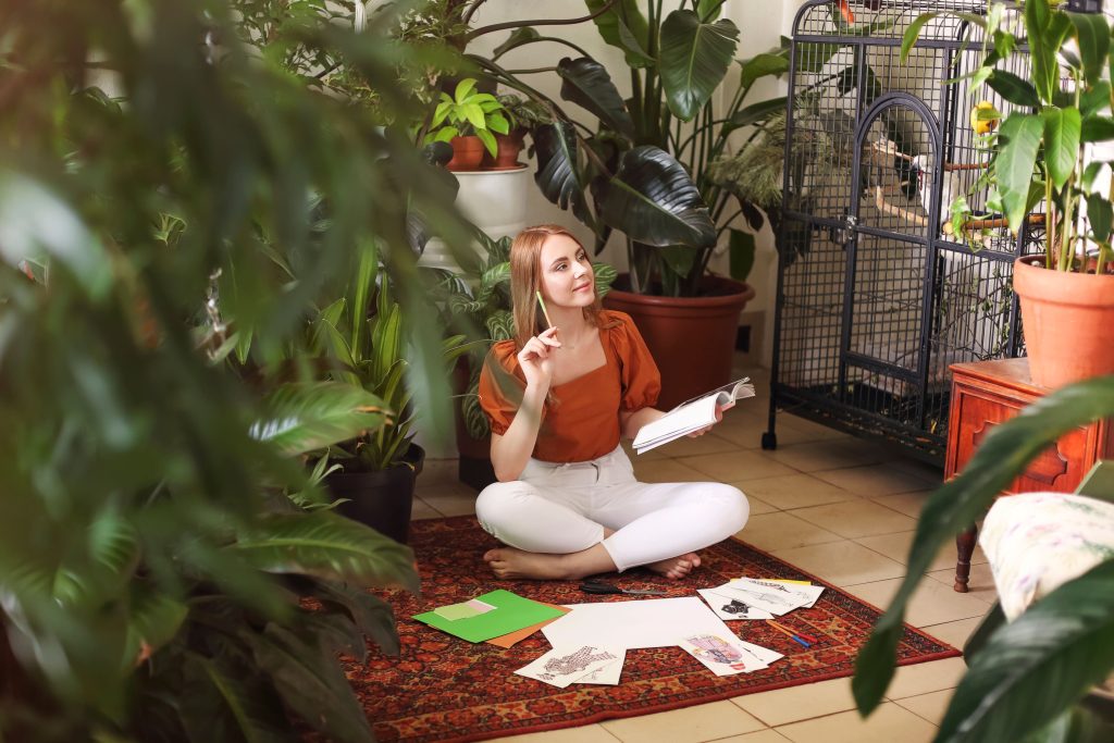 A young red-haired woman creating her Feng Shui wish maps while sitting on a boho-style carpet.